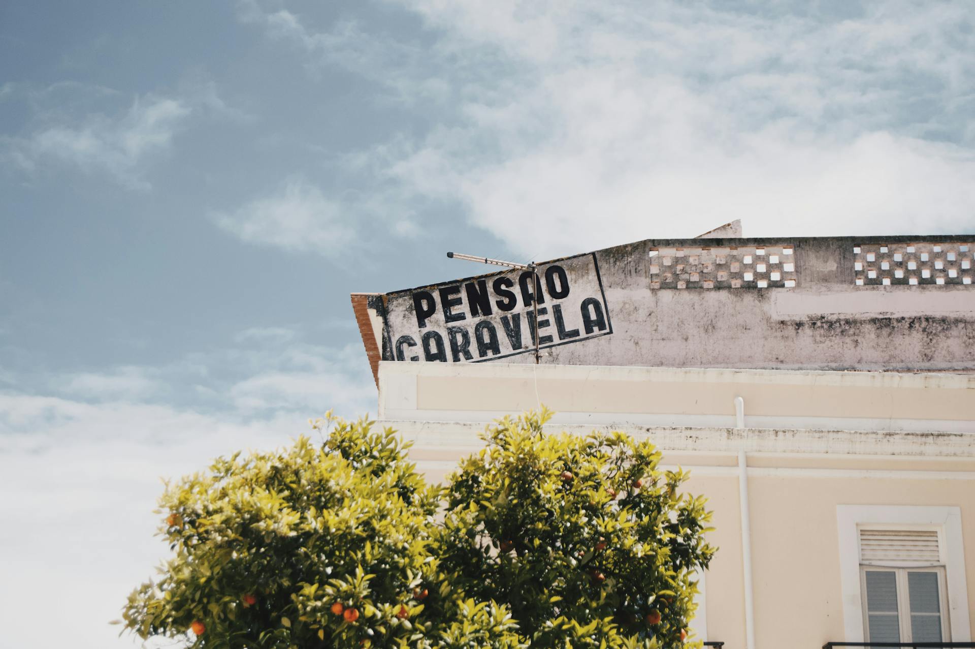 Rustic Pension Caravela sign atop a sunny building with orange trees.