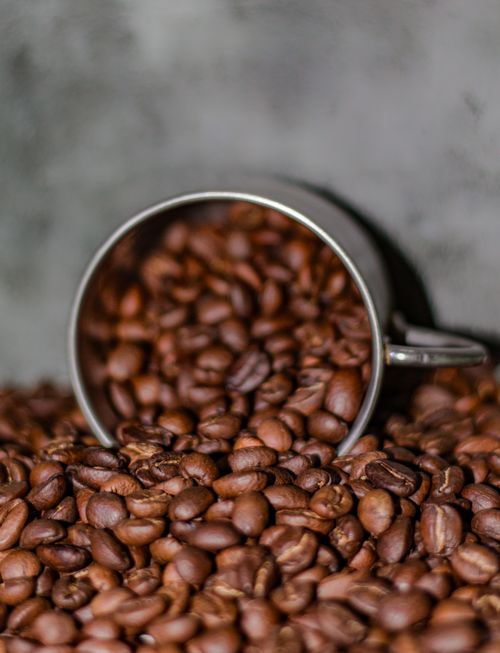 Free A close-up of roasted coffee beans spilling from a metal cup, ideal for coffee-themed designs. Stock Photo