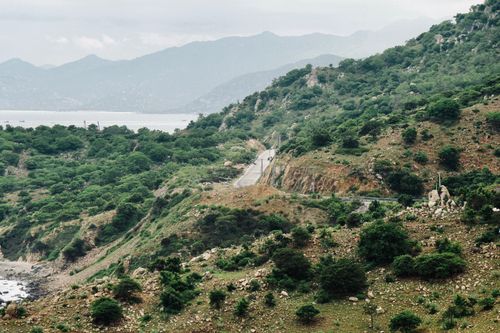 Free A tranquil road winds through lush green hills, overlooking a scenic water and mountain landscape. Stock Photo