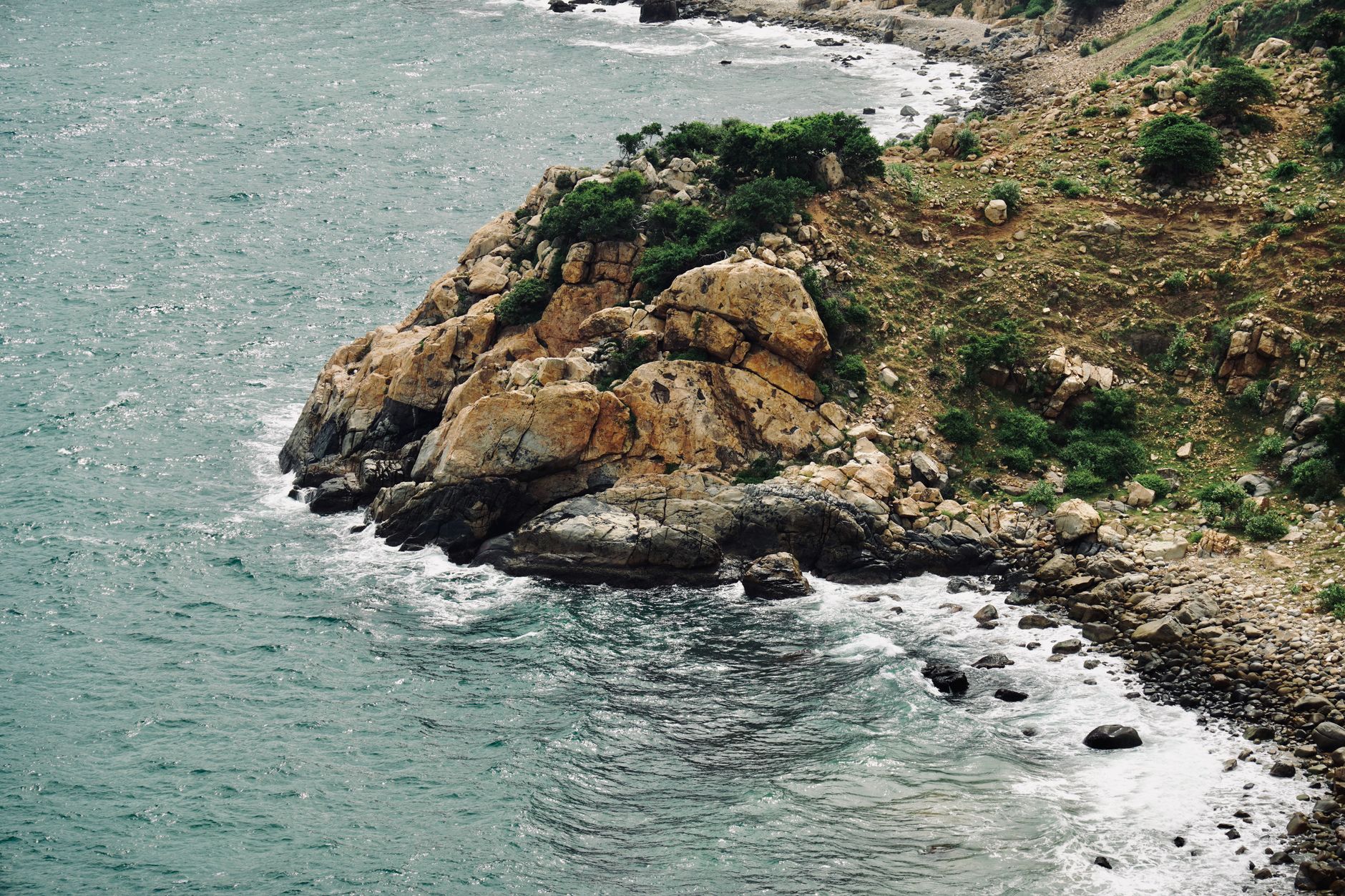 A picturesque rocky coastline with waves crashing against the shore under a clear day sky.