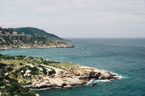 Free A serene view of a rocky coastline overlooking a clear blue ocean under a cloudy sky. Stock Photo