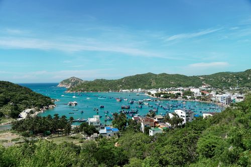 Free Aerial view of a picturesque fishing village and harbor with boats. Lush greenery and mountains surround the area. Stock Photo