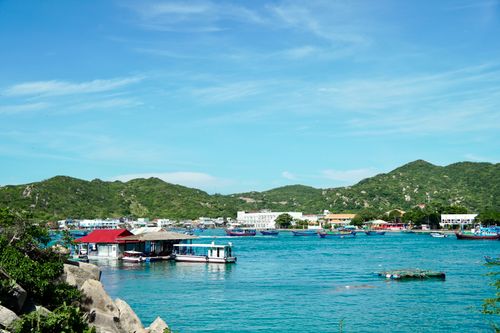 Free Picturesque coastal village with boats, hills, and clear blue sky, ideal for travel inspiration. Stock Photo