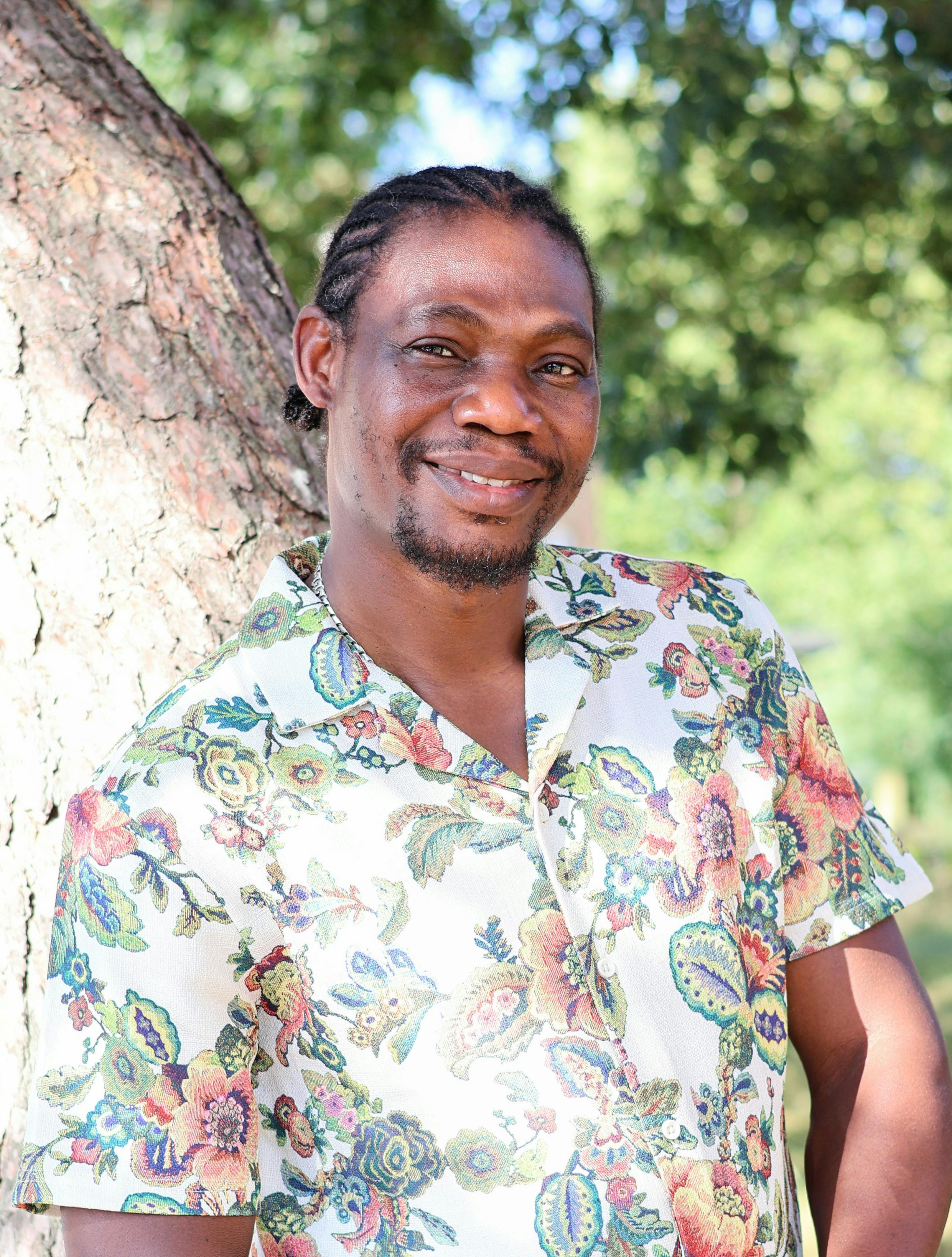 Smiling man in floral shirt outdoors by tree, enjoying nature.