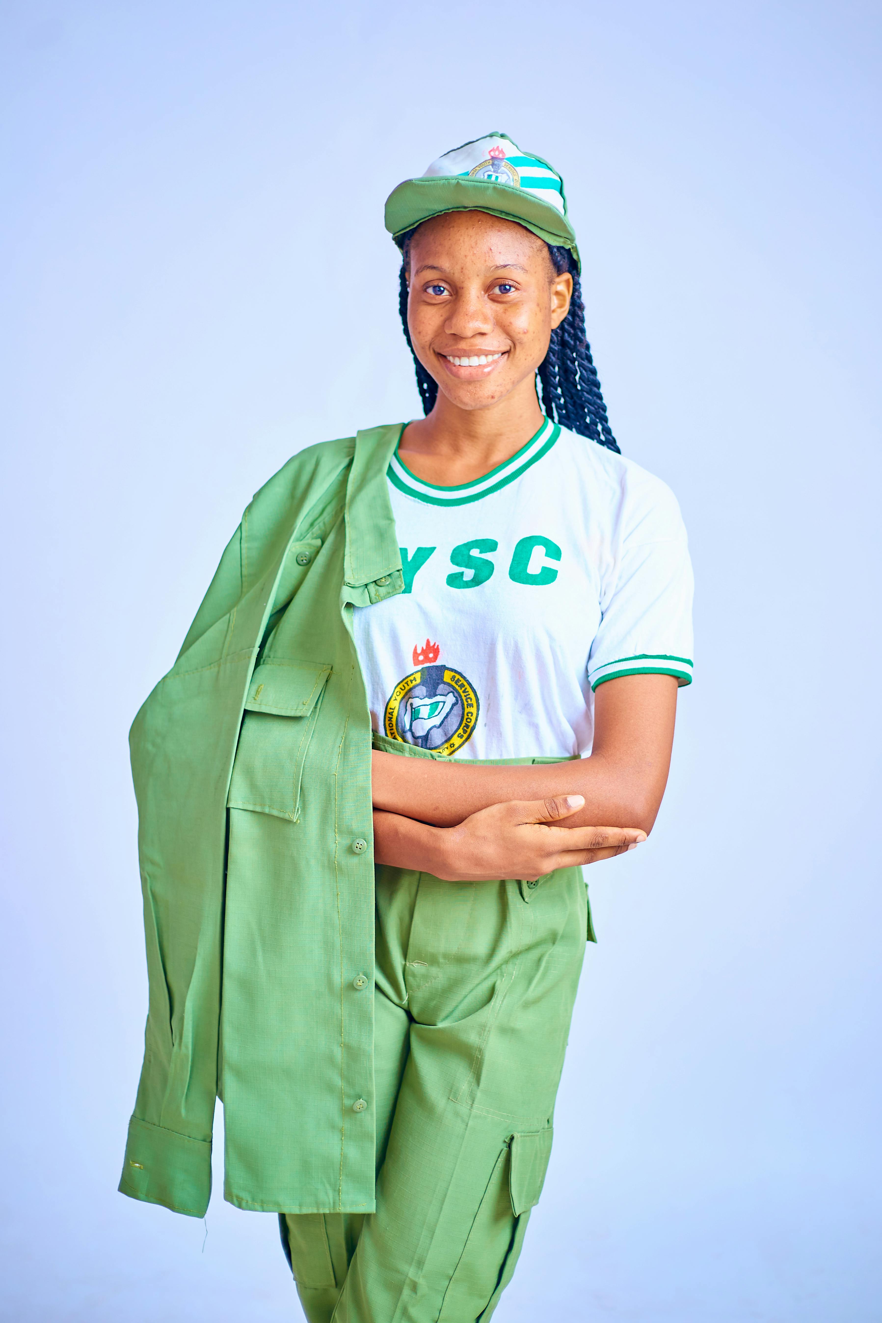 Vibrant portrait of a woman in Nigerian NYSC uniform against a light background.