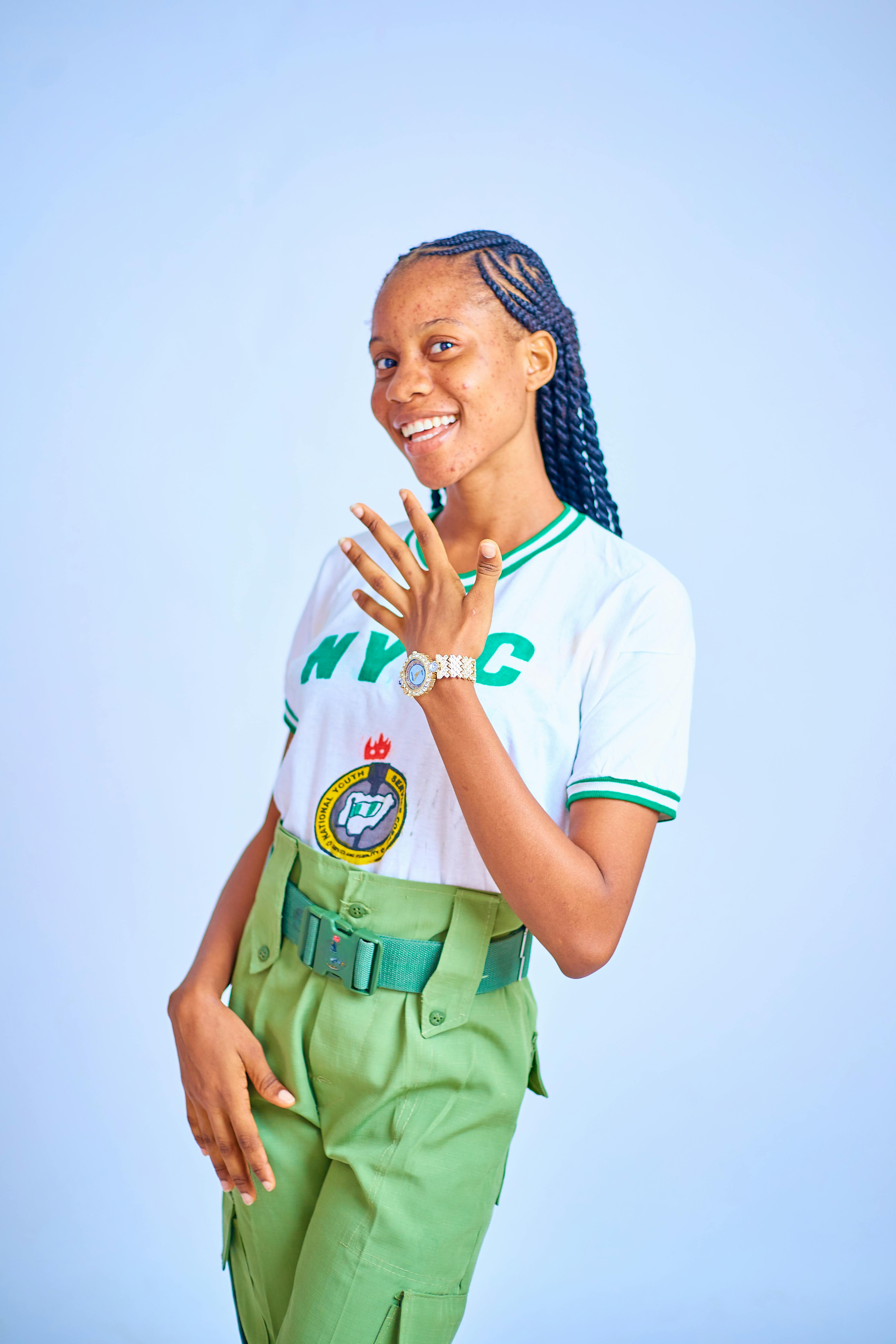 Vibrant portrait of a young woman in NYSC uniform against a light background, smiling confidently.