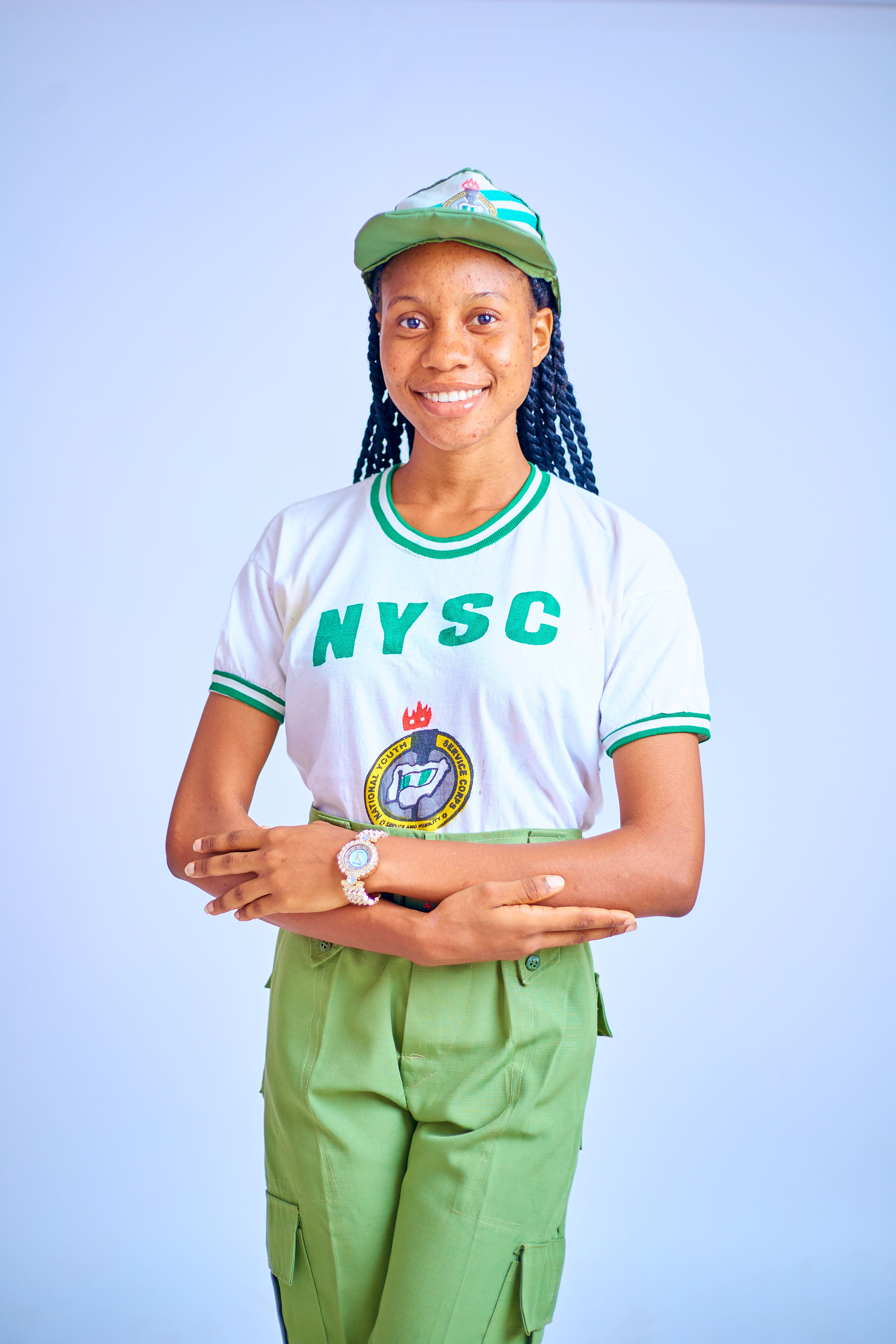 Portrait of a smiling young adult in NYSC uniform against a plain background.