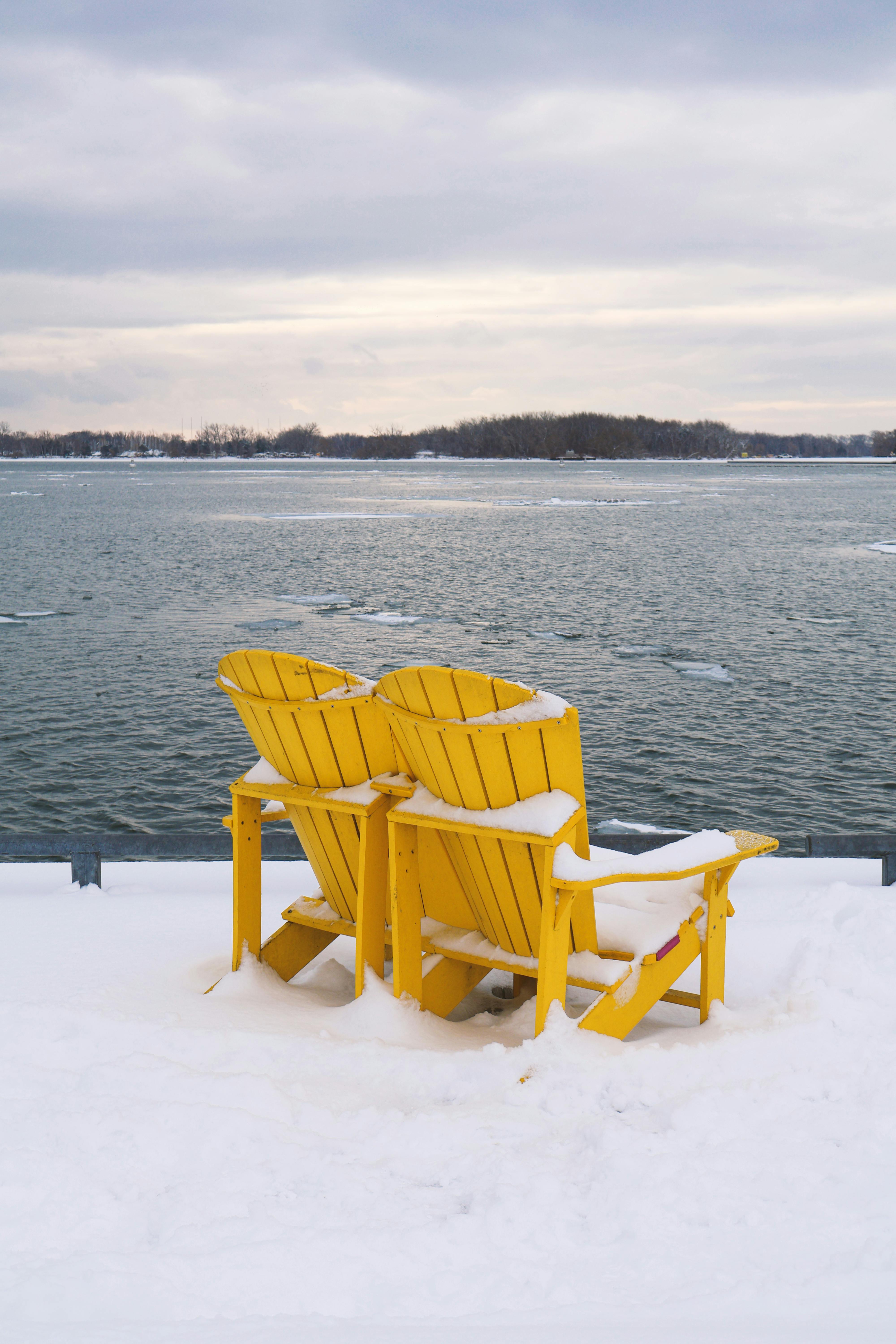Two yellow Muskoka chairs covered in snow overlooking a serene Lake Ontario in Toronto.