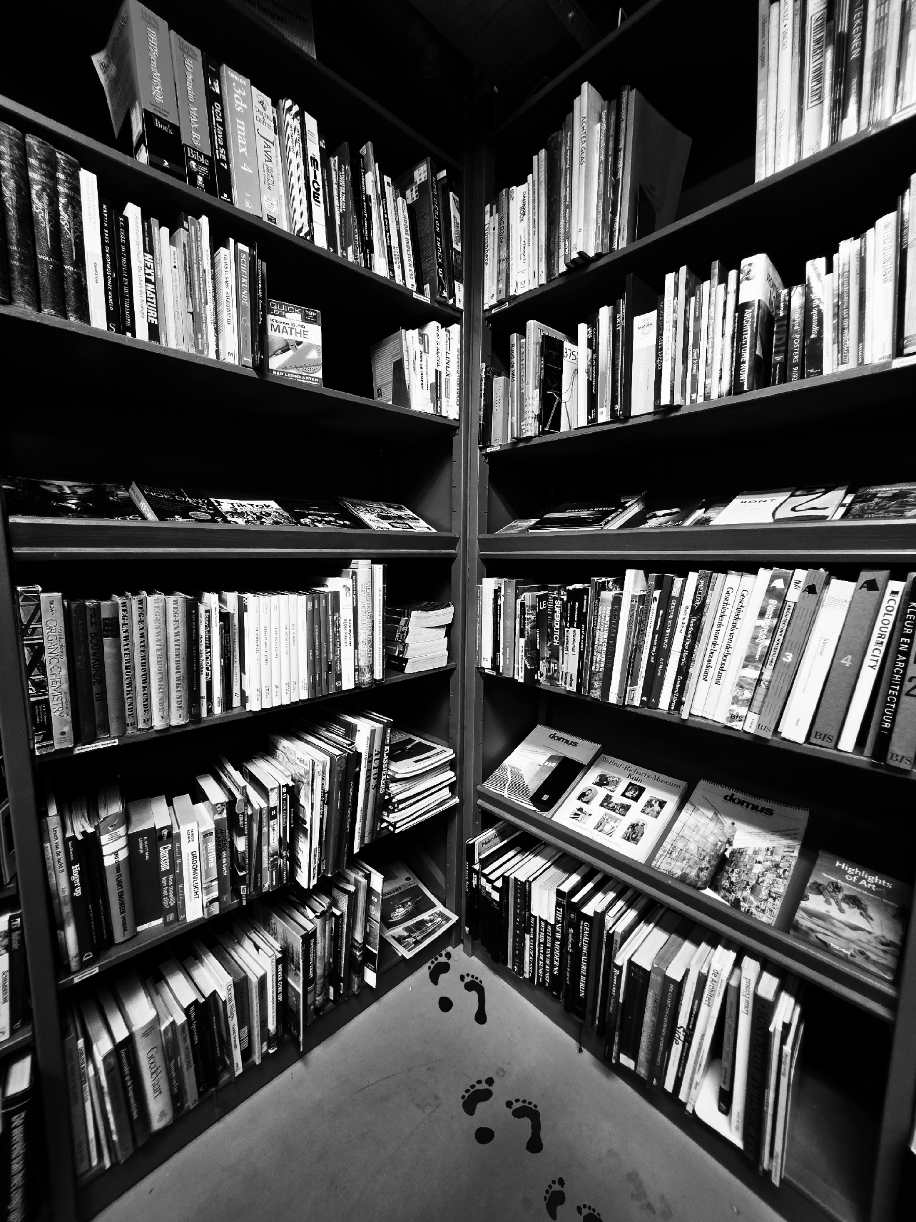 Free A captivating black and white photo of a filled corner bookshelf in a Dutch library. Stock Photo