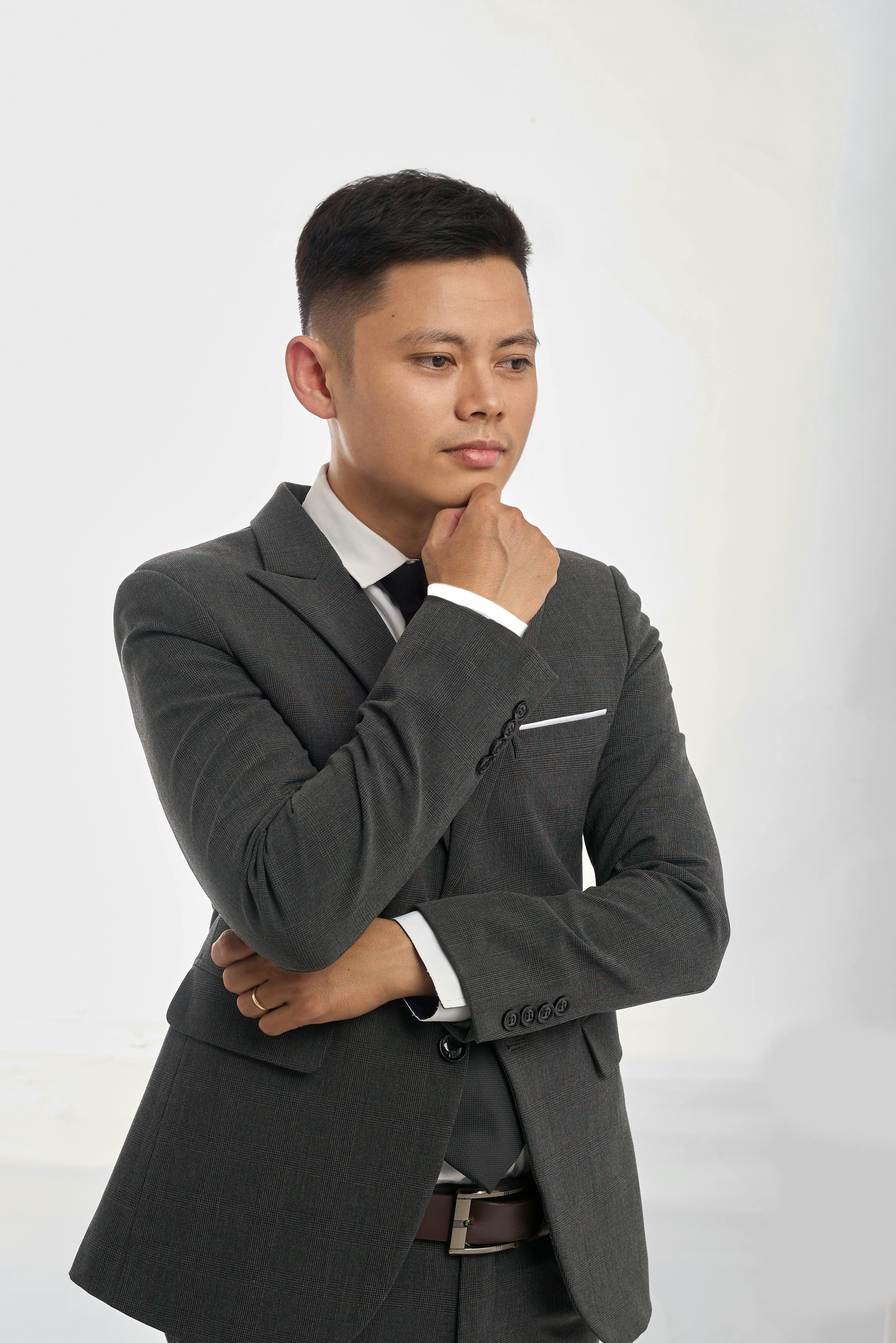 Ilmainen Pukuun pukeutunut mies poseeraa mietteliäästi yksinkertaista taustaa vasten. Kuvapankkikuva