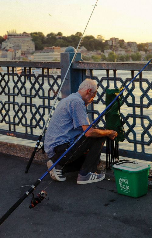 Free Elderly man fishing on Galata Bridge with sunset view of Istanbul in the background. Stock Photo
