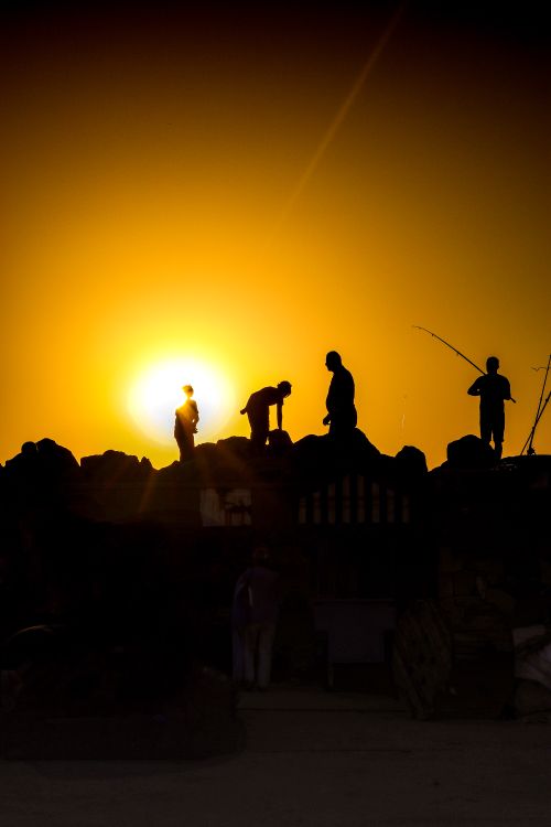 Free Silhouettes of people enjoying a vibrant sunset at a rocky shore. Stock Photo