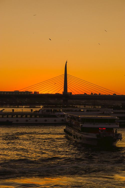 Free A stunning sunset scene with a boat on the river and a bridge silhouette against a vibrant orange sky. Stock Photo