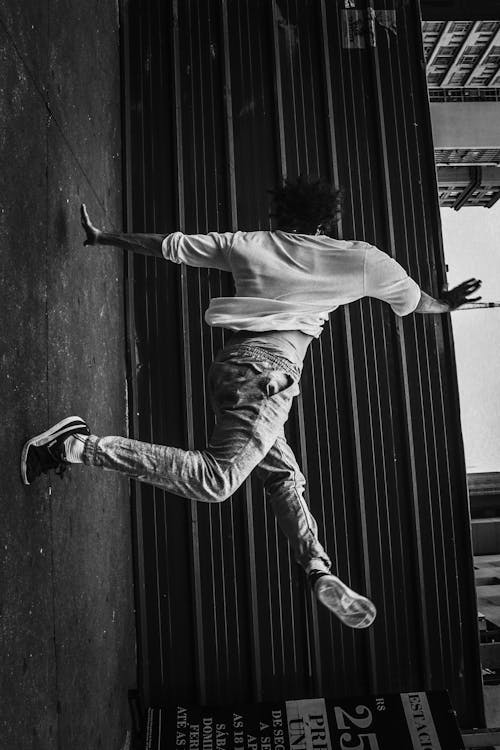 Man in White Shirt and Gray Pants Jumping on Black Wooden Wall