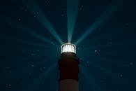 灯塔在星光熠熠的夜空中发出光芒，在大海上空产生空灵的光芒