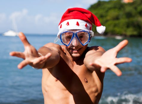 Man in Santa hat and snorkel mask reaches out playfully on a tropical beach.