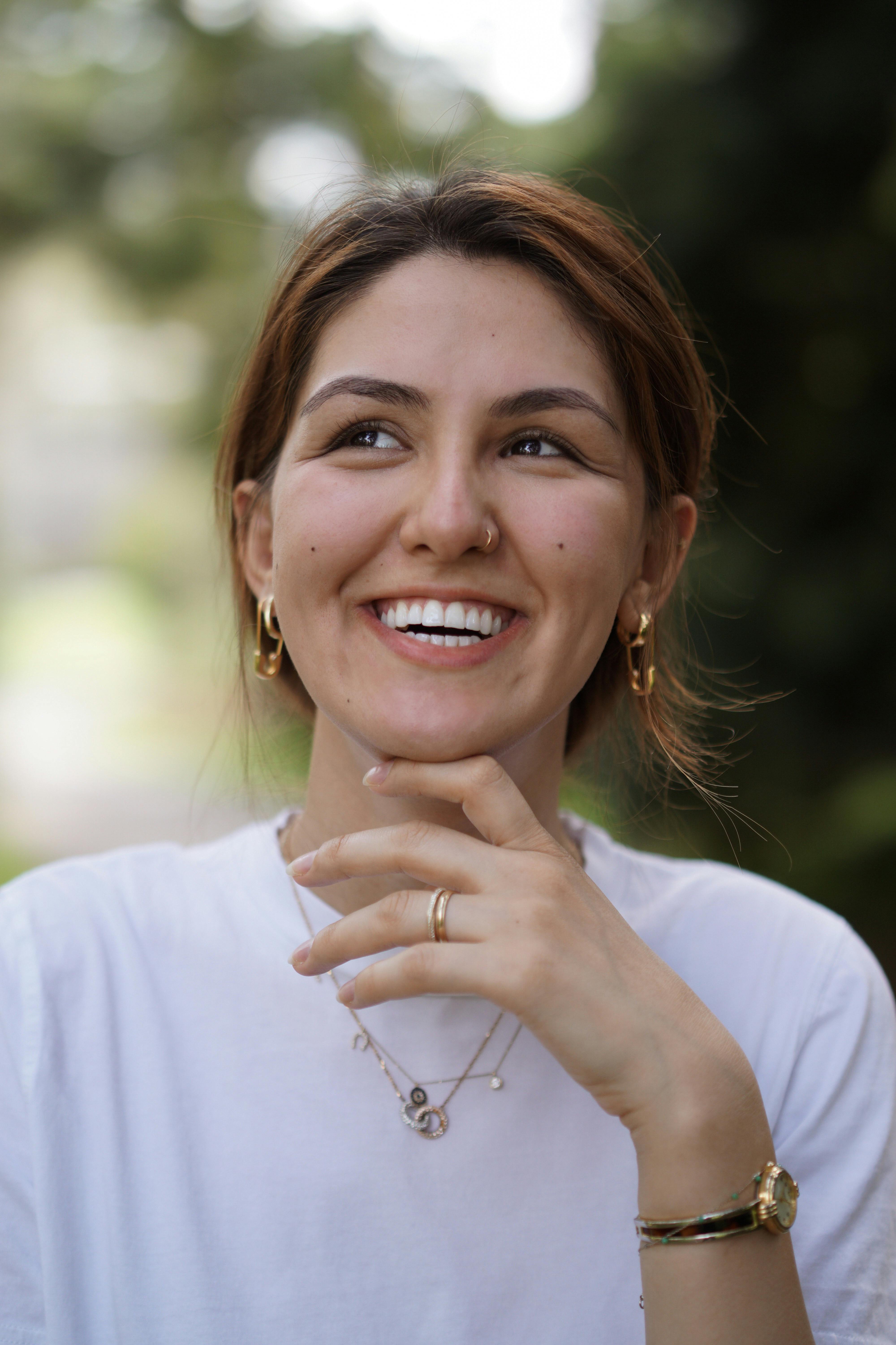 Cheerful young woman smiling in a natural outdoor setting, wearing white shirt.