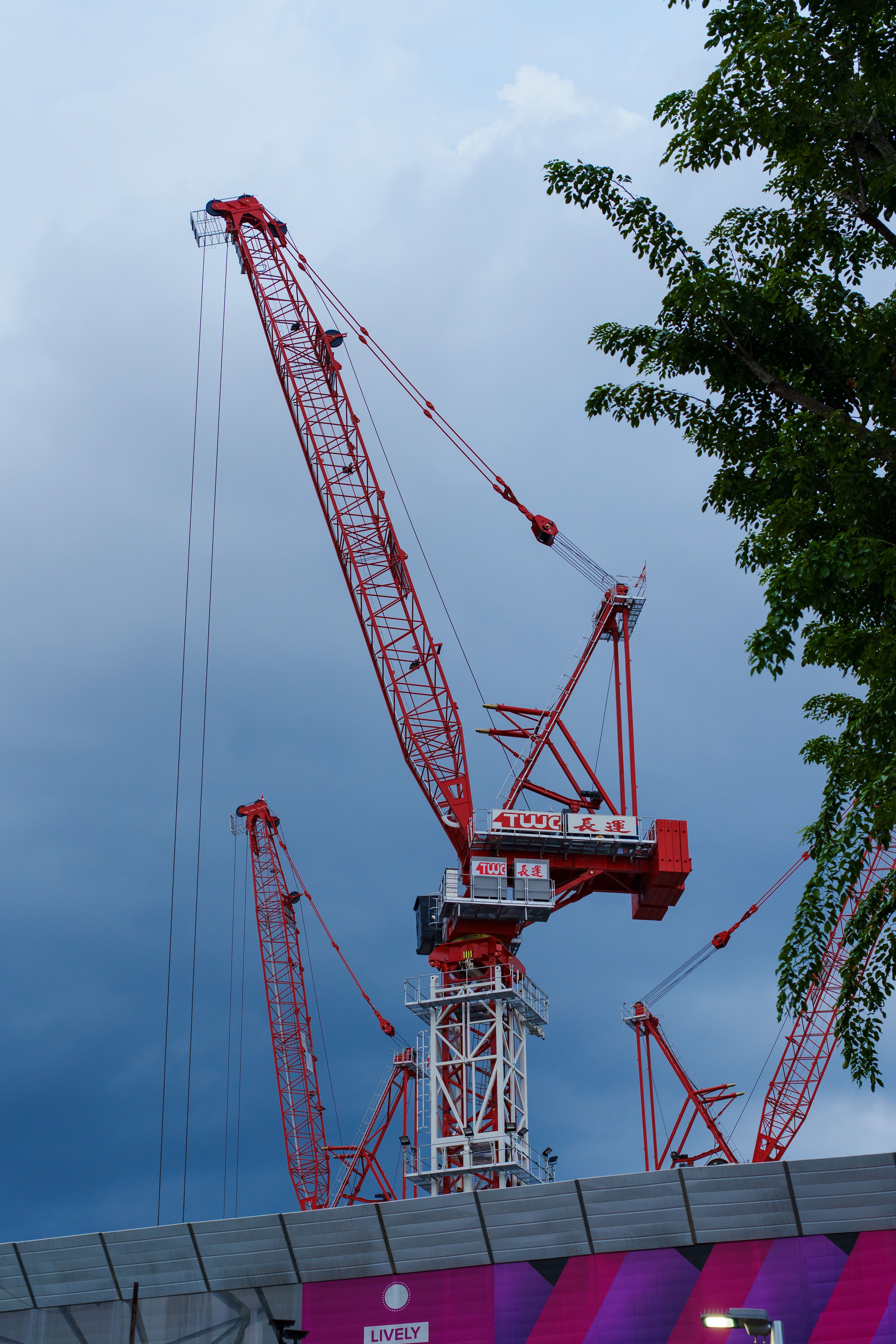 Red tower cranes silhouetted against a dramatic blue sky with clouds.
