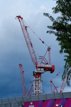 Red tower cranes silhouetted against a dramatic blue sky with clouds.