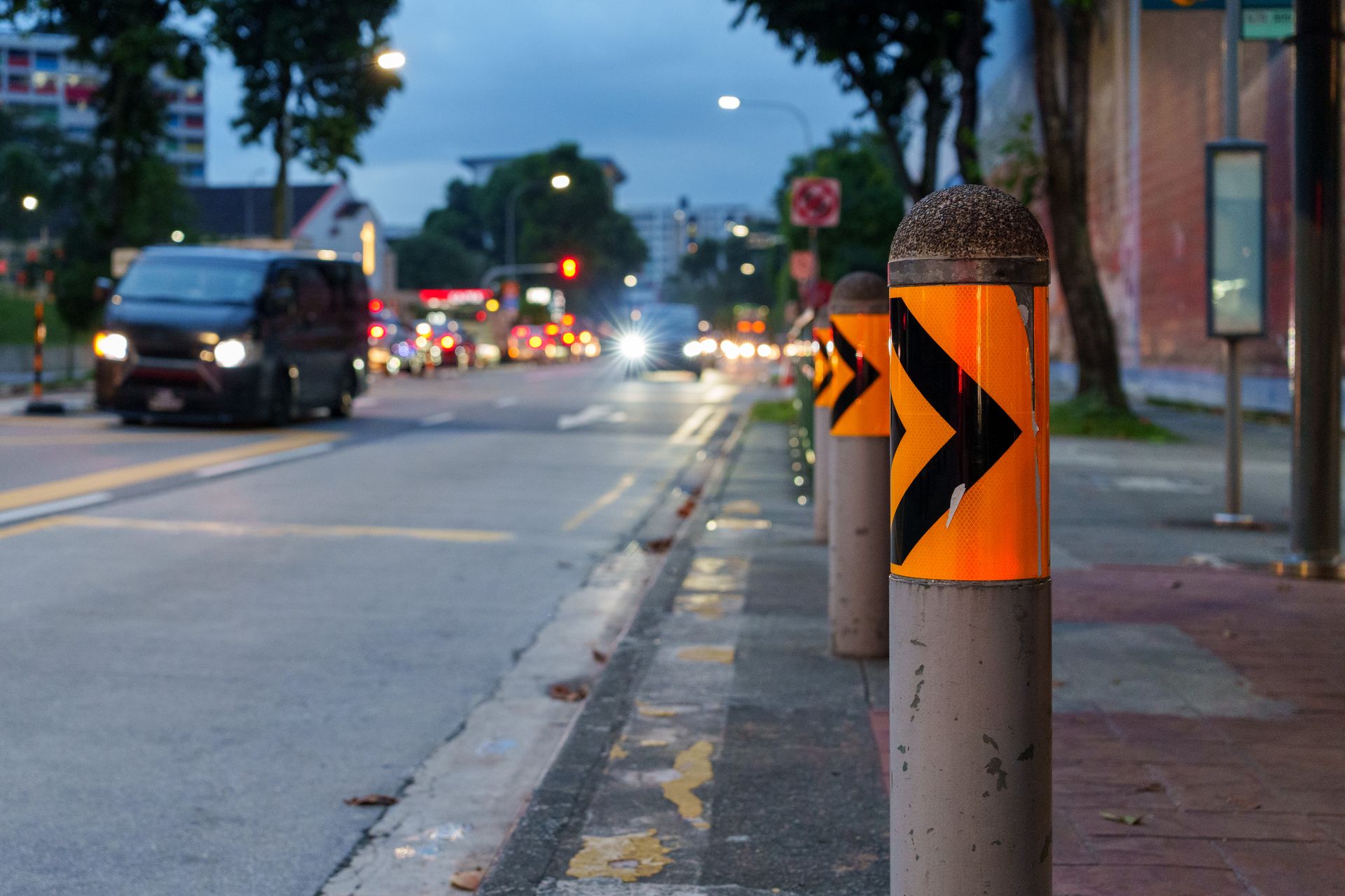 City street scene featuring reflective bollards and traffic as evening lights begin to illuminate the area.