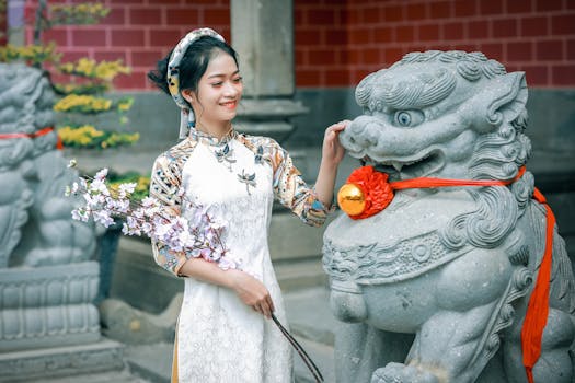 A smiling woman in an ao dai interacts with a stone lion in Vietnam.