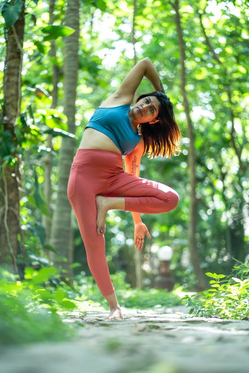 Free A woman in vibrant workout attire practices yoga in a serene forest environment, showcasing flexibility and balance. Stock Photo