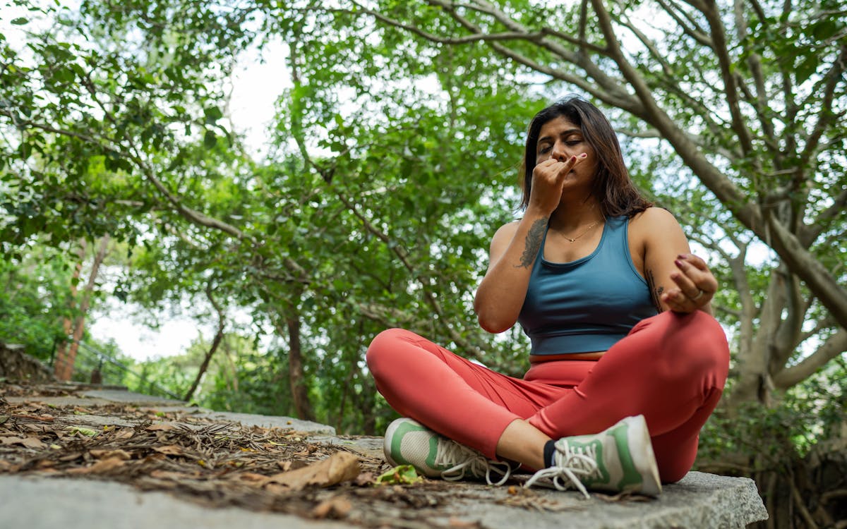 Young woman meditating in a forest, practicing yoga breathing exercises on a stone platform.