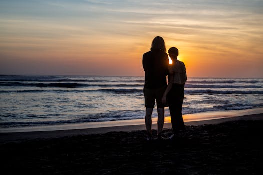 日落时分，一对夫妇站在巴厘岛海滩上，浪漫的轮廓映衬着海景