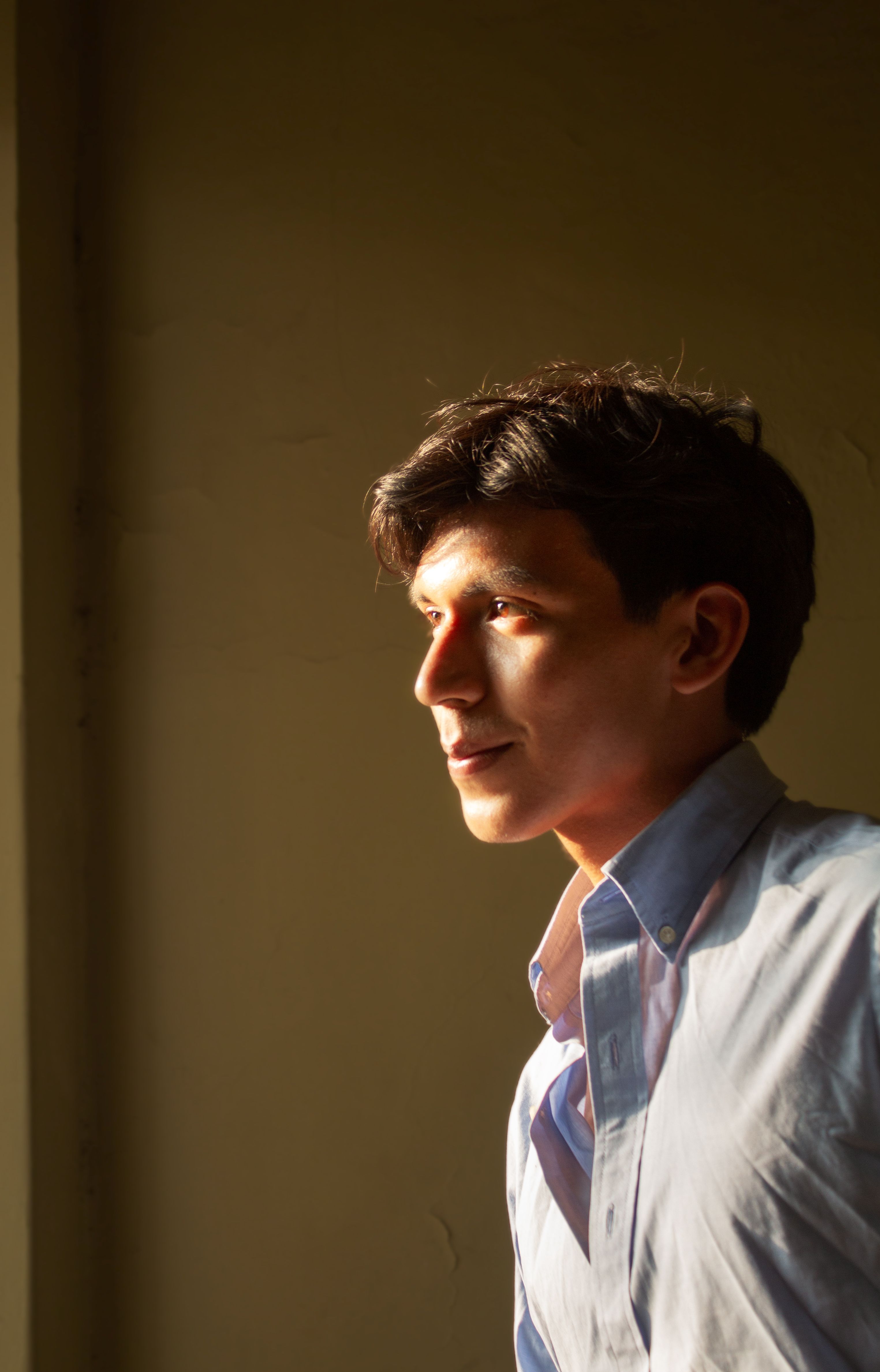 Portrait of a young man looking away, lit by warm sunset light indoors.