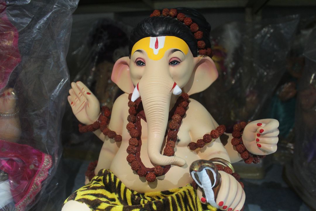 Ganesh Chaturthi 2026: Modak Traditions and Gujarat's Ganeshotsav Food Culture 2 A close-up of a hand-painted clay Ganesha idol displayed among other idols wrapped for sale