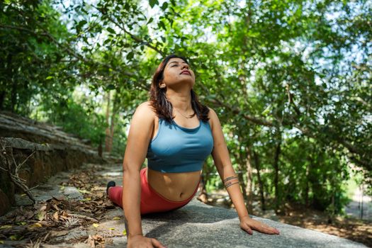 A woman practicing yoga poses amidst greenery in a sunlit outdoor park setting.