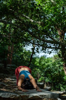 Woman practicing yoga outdoors on stone steps, surrounded by lush greenery.