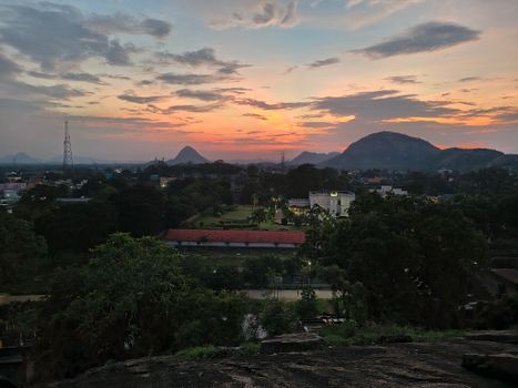 Dramatic sunset over a lush landscape with mountains and cityscape in the distance.