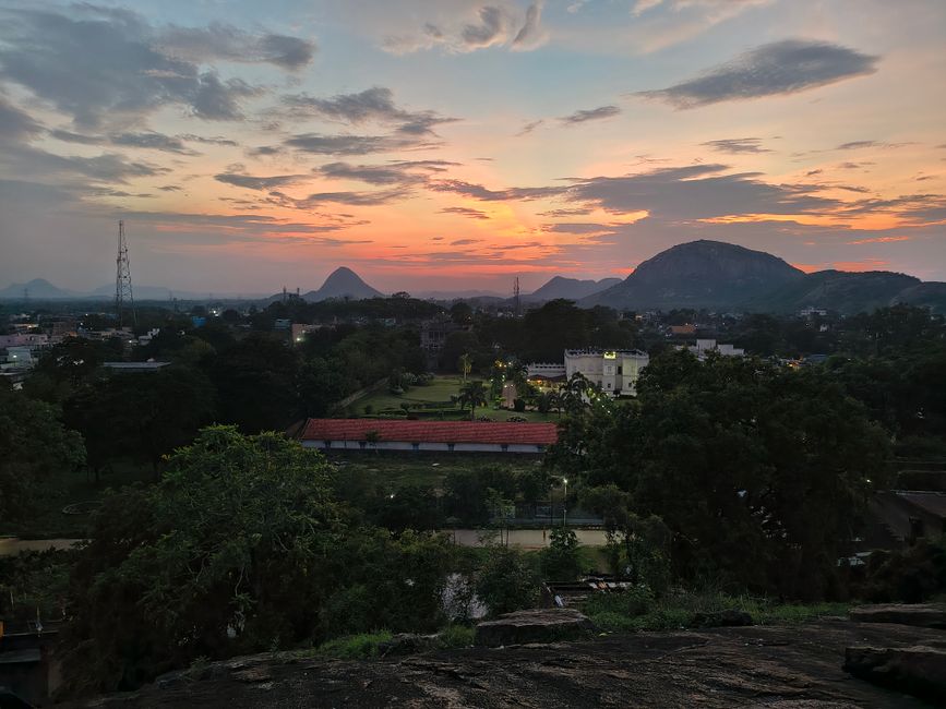 Dramatic sunset over a lush landscape with mountains and cityscape in the distance.