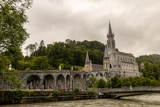 Historic cathedral in Lourdes, France amid lush greenery and stone architecture.