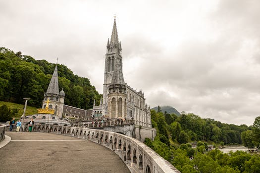 View of the iconic Basilica of Lourdes surrounded by lush greenery under a cloudy sky.