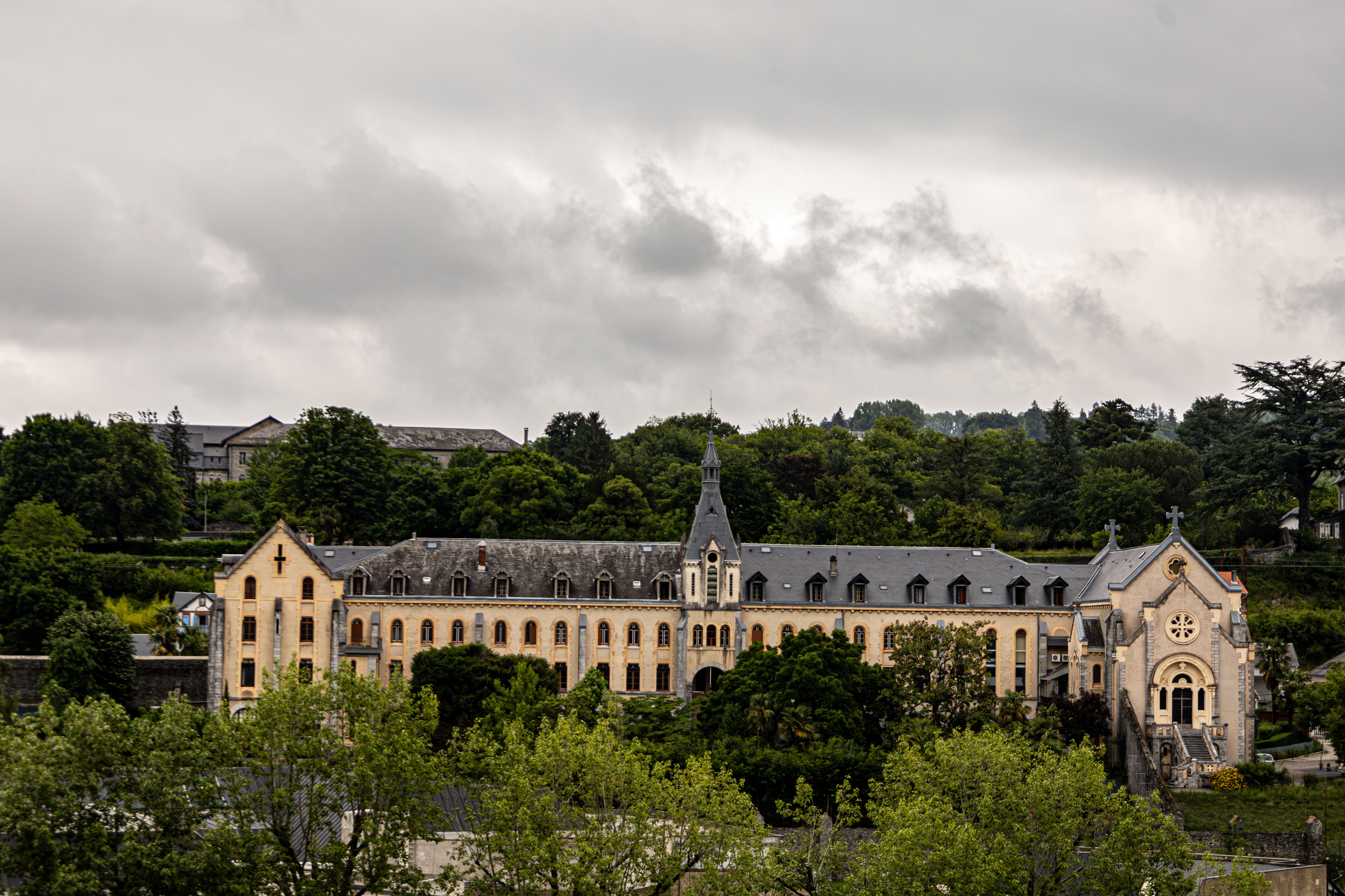 Elegant historic building set against lush greenery and cloudy sky, showcasing Gothic architectural style.