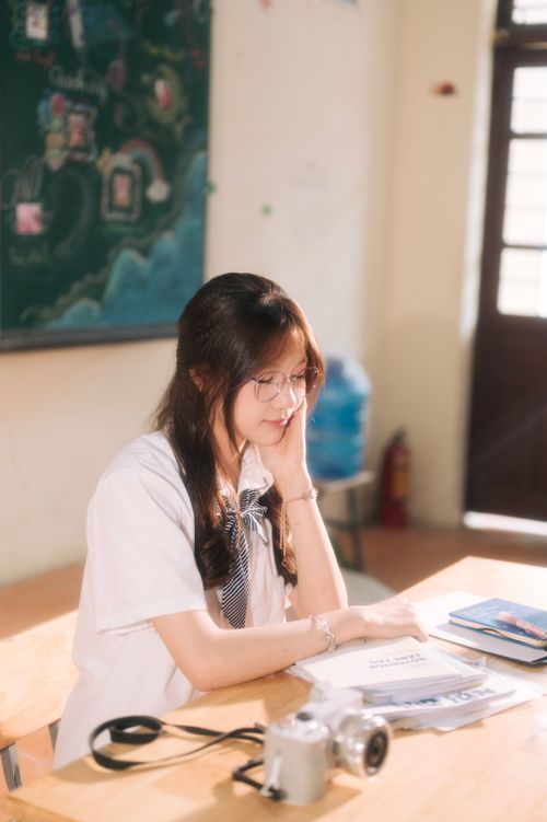 Free Focused student studying at a desk with books and camera in a bright classroom. Stock Photo