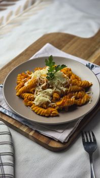 Plate of fusilli pasta topped with tomato sauce and cheese, garnished with herbs, set on a wooden board.