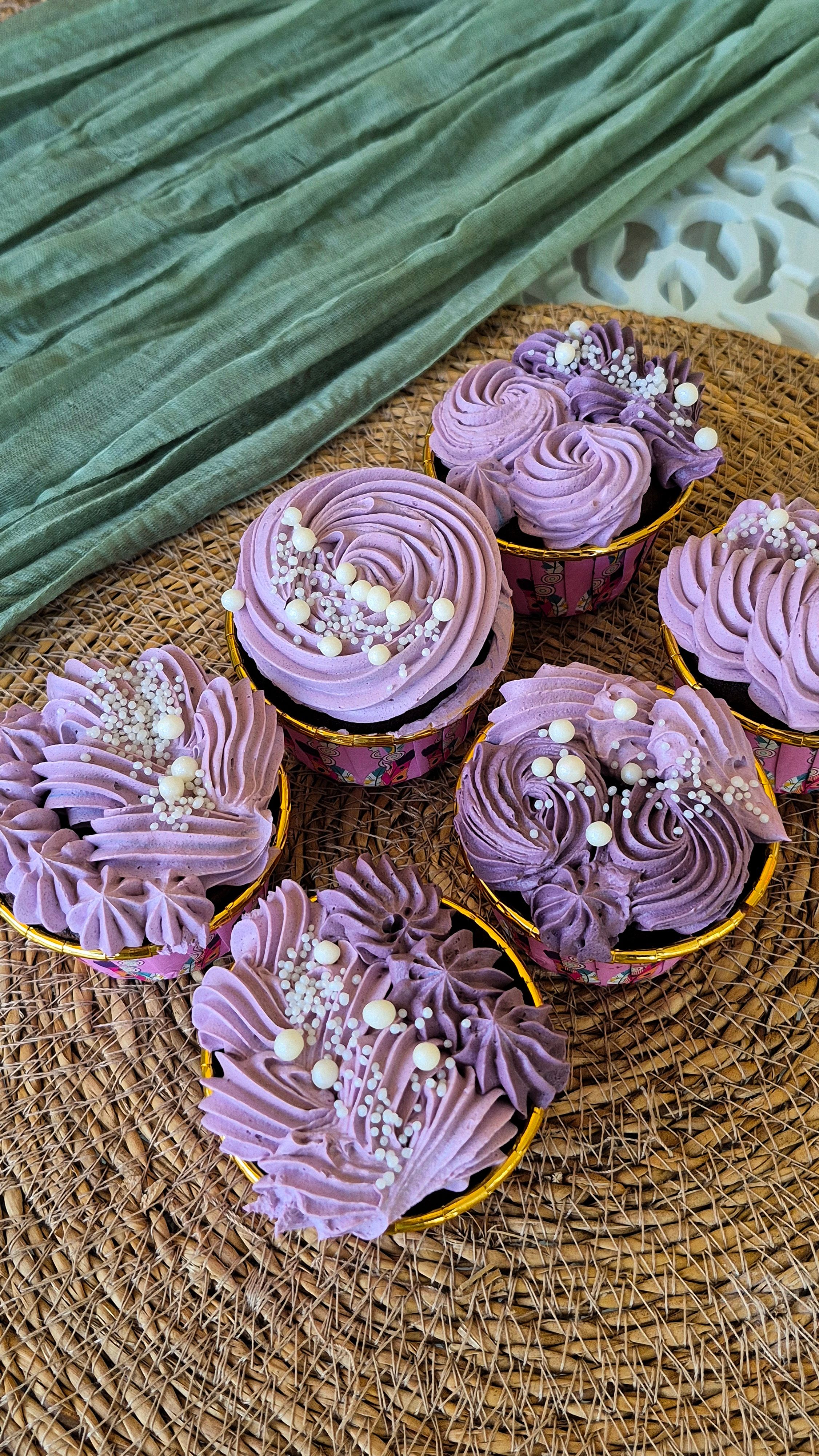 Artistic cupcakes with lavender frosting and sprinkles on a textured mat.