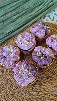 Artistic cupcakes with lavender frosting and sprinkles on a textured mat.