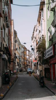 Charming narrow city street lined with colorful residential buildings and vehicles parked along the sides.