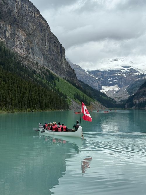 Free Group canoeing on Lake Louise, Alberta with snow-capped mountains and Canadian flag. Stock Photo