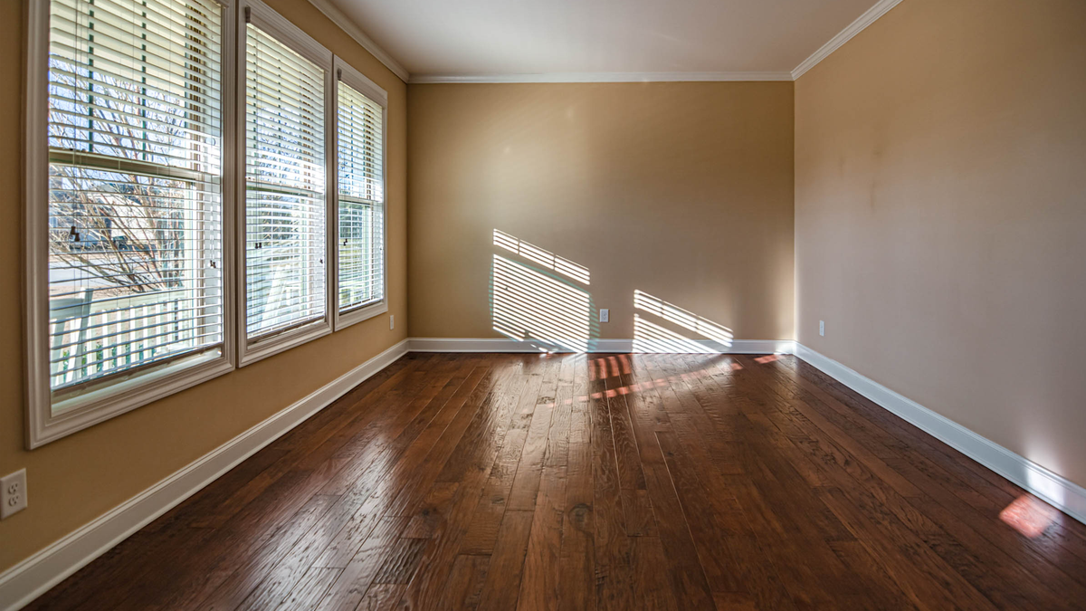 Sunlit empty room with hardwood floors and large windows, ideal for home staging.