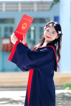 Happy young woman in graduation gown with diploma, celebrating success outdoors.