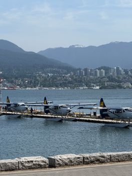 Seaplanes docked by the Vancouver waterfront with city skyline and mountains in the background.