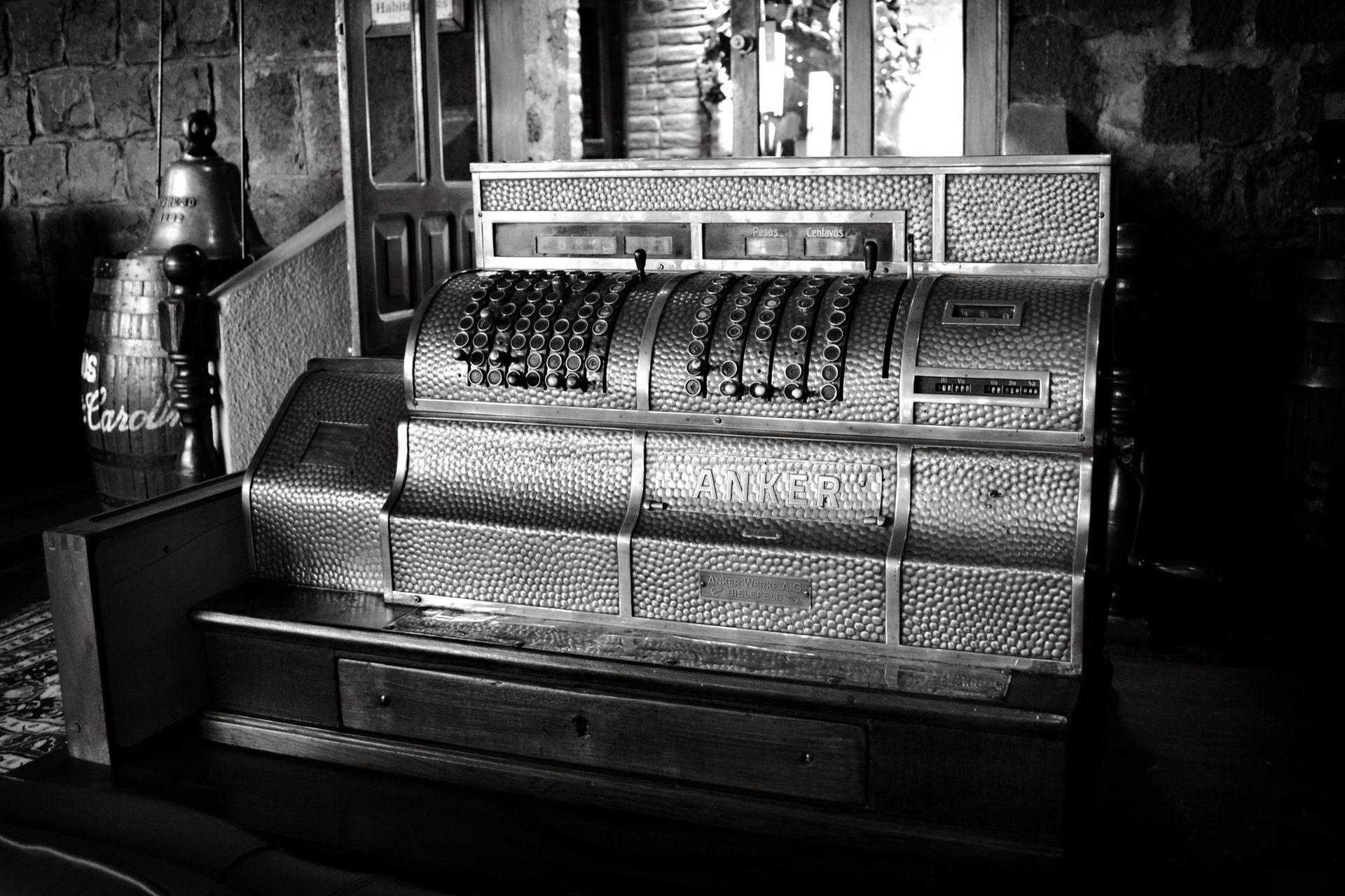 Black and white photo of a vintage Anker cash register in a rustic interior setting.