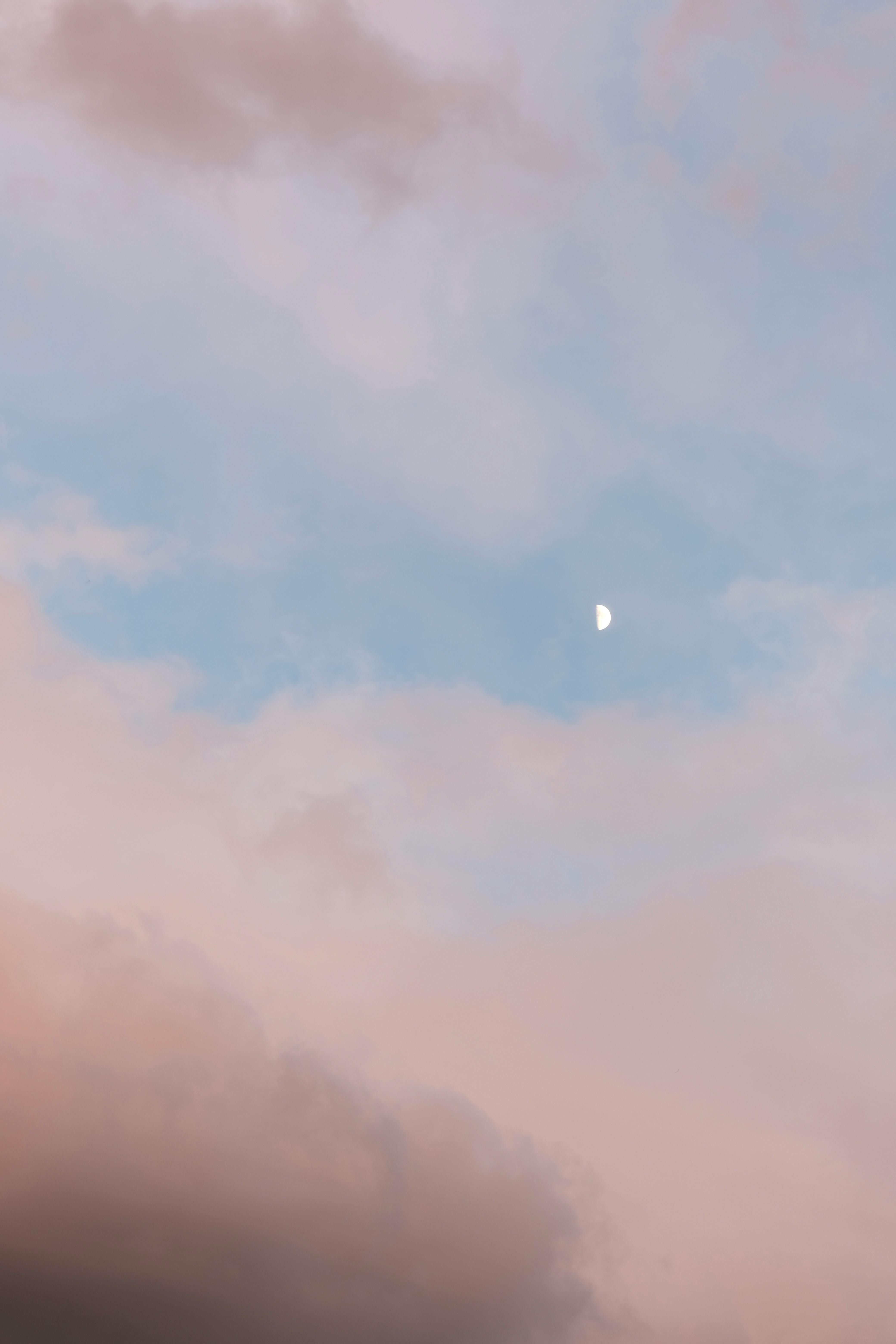 Serene sky with pastel clouds and a half moon at twilight.