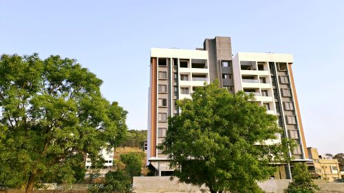 Free A tall, modern apartment building surrounded by green trees under a clear blue sky. Stock Photo