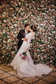 新婚夫妇在充满活力的花卉墙前浪漫亲吻，尽显爱与优雅